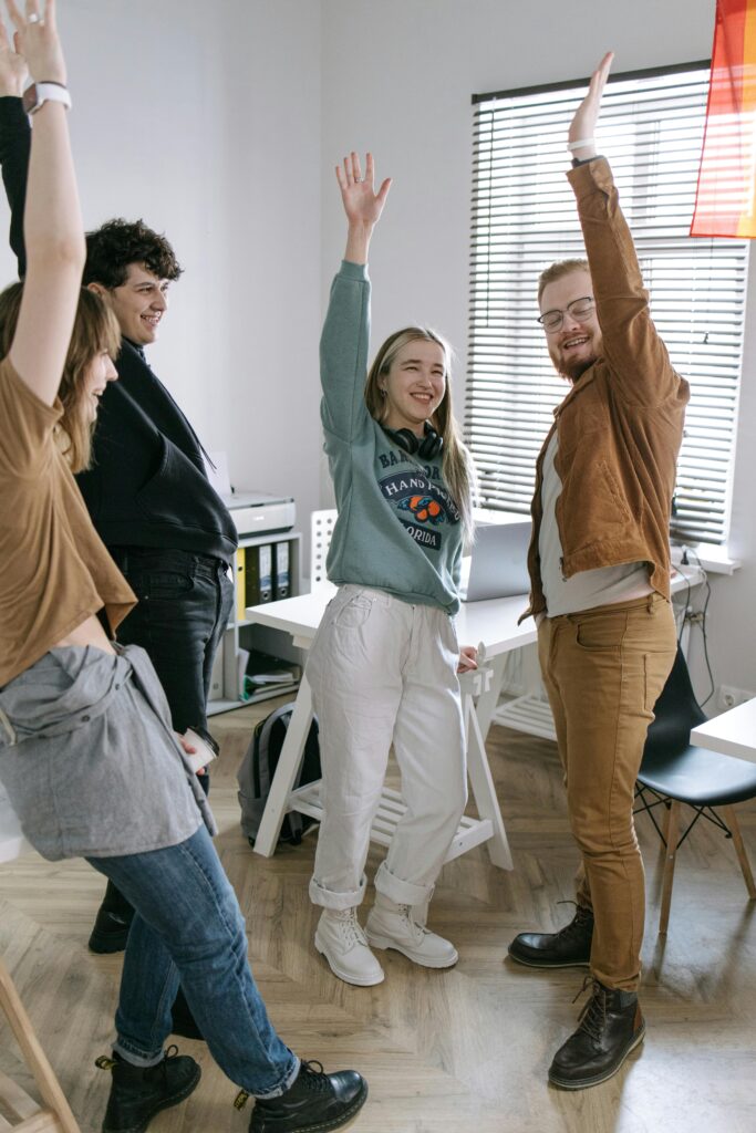 A joyful, diverse group of young adults celebrating in an office space, embodying teamwork and success.